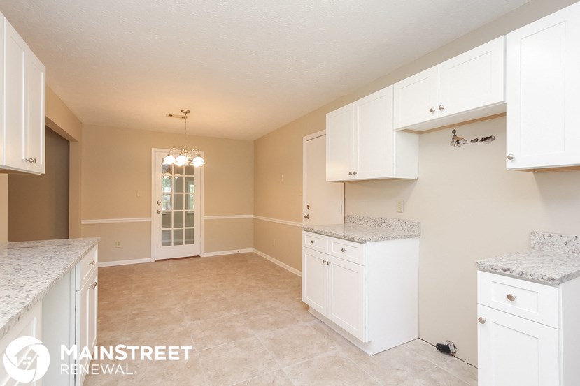 a kitchen with white cabinets and counters and a door to the living room