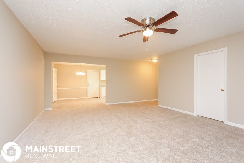 a spacious living room with carpet and a ceiling fan