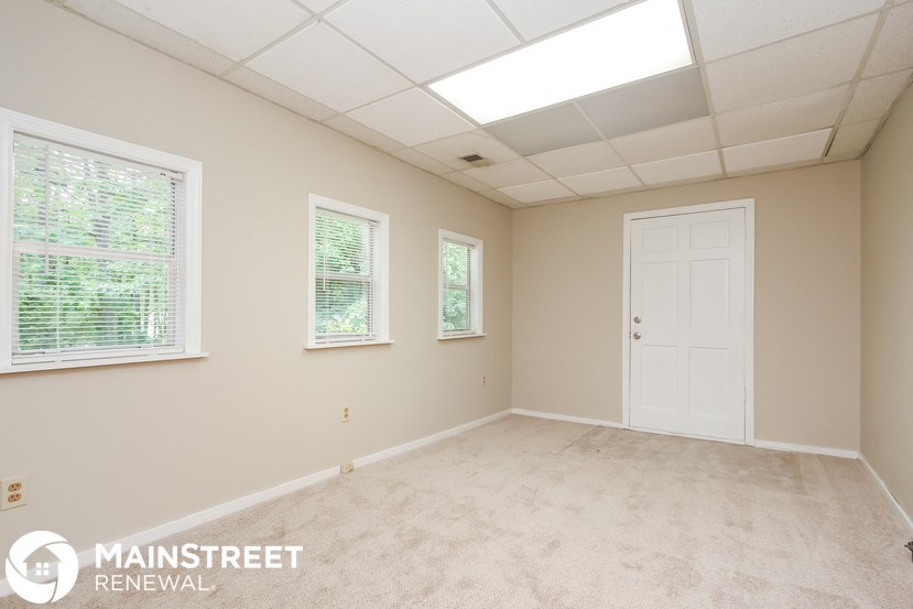 an empty room with a white door and three windows