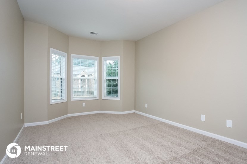 a spacious living room with three windows and a carpeted floor