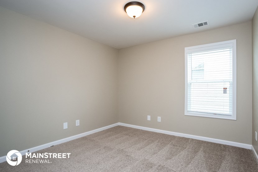 the spacious bedroom with carpeted flooring and a large window