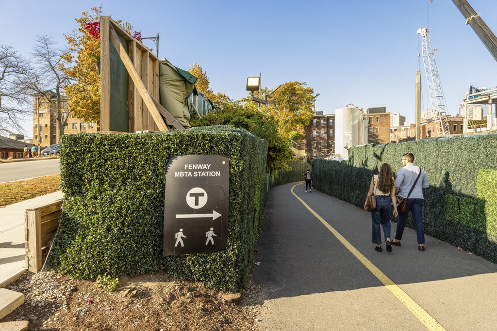 A sign on a hedge indicates the direction to the MBTA station.