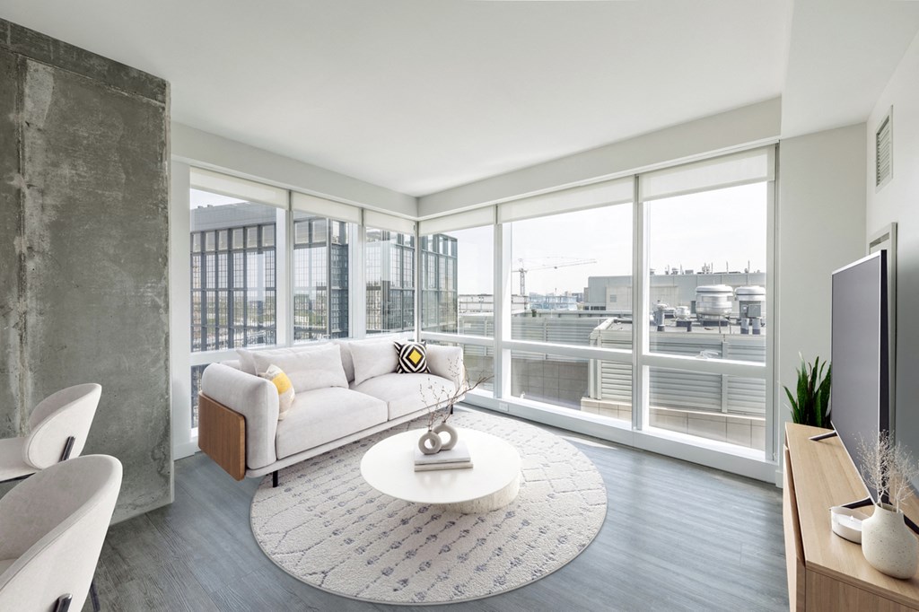 A modern living room with a white sofa and a large window overlooking the city.