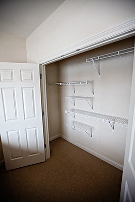 an empty closet with a white door and white shelves on the wall