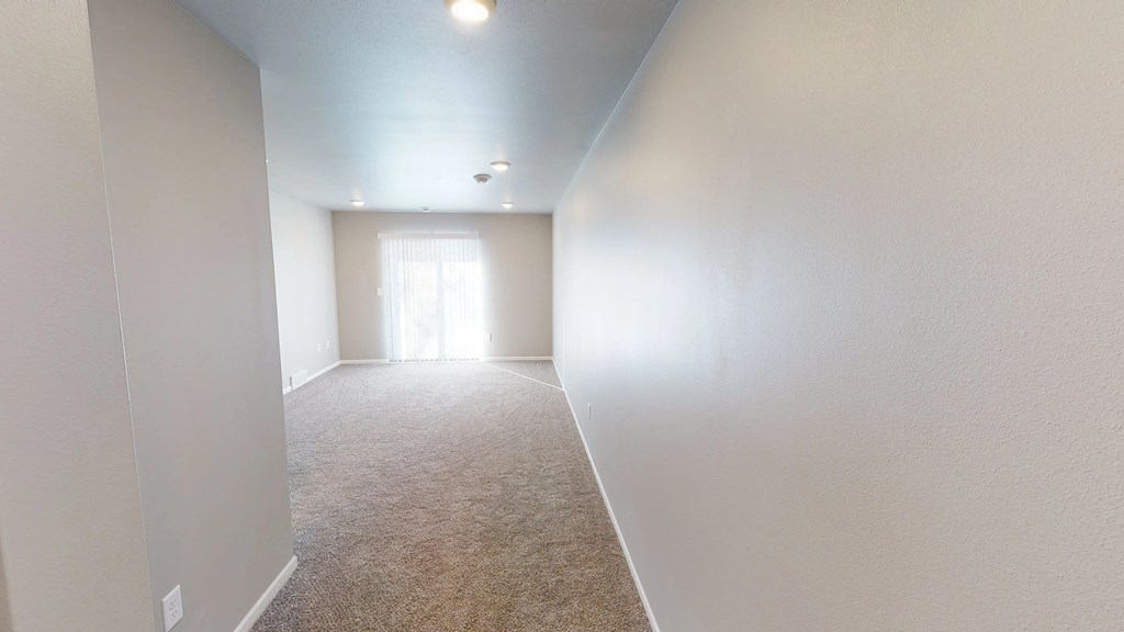 an empty room with white walls and carpet and a door to a bedroom