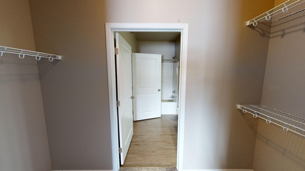 a walk in closet with a door open to a hallway with shelves and a closet