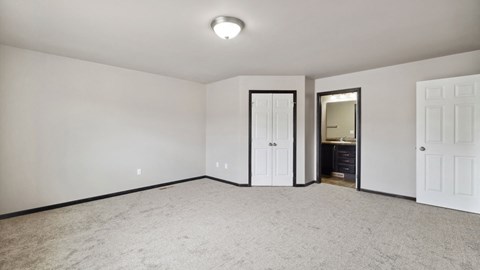 A room with white walls and carpeted floor with a doorway leading to another room.