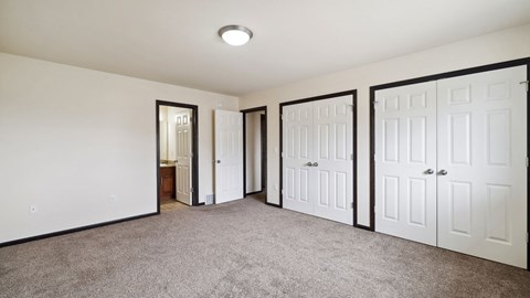 A room with white walls and carpeted floor with three white doors.