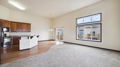 A spacious living room with a kitchen area and a large window overlooking a balcony.