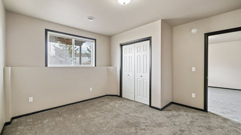 A room with a carpeted floor and a window with a view of trees.