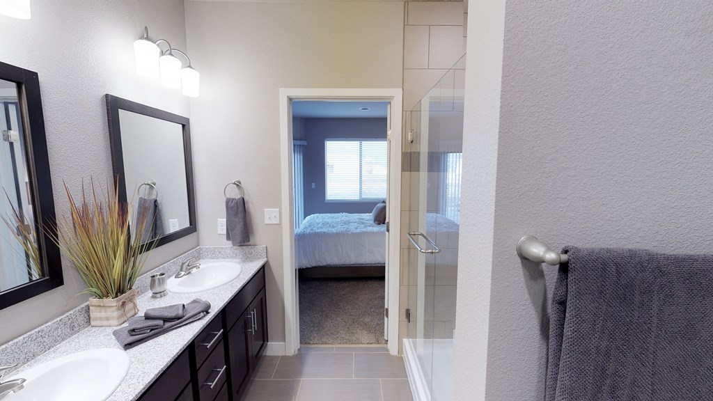 a bathroom with two sinks and a shower and a bedroom