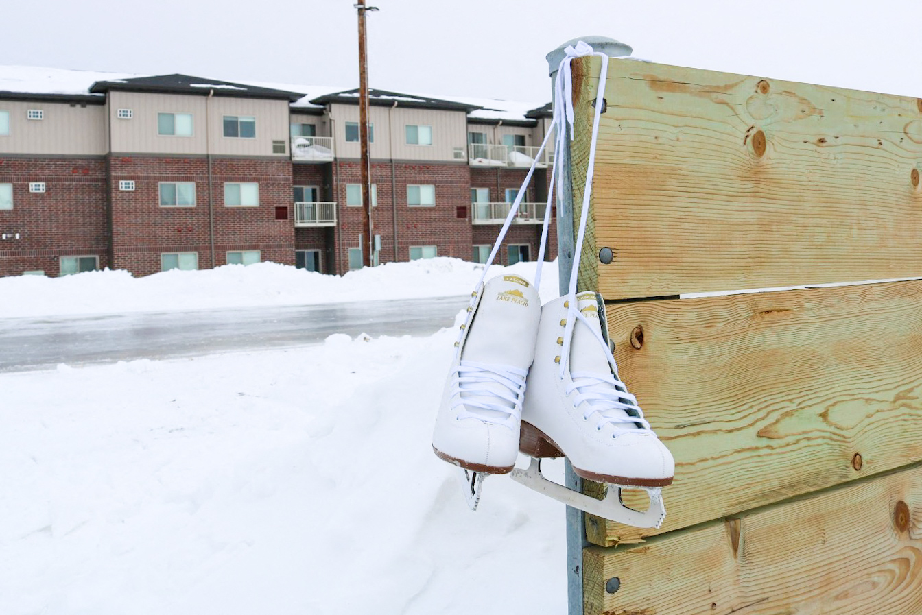 a pair of ice skates hanging on a wooden fence in the snow