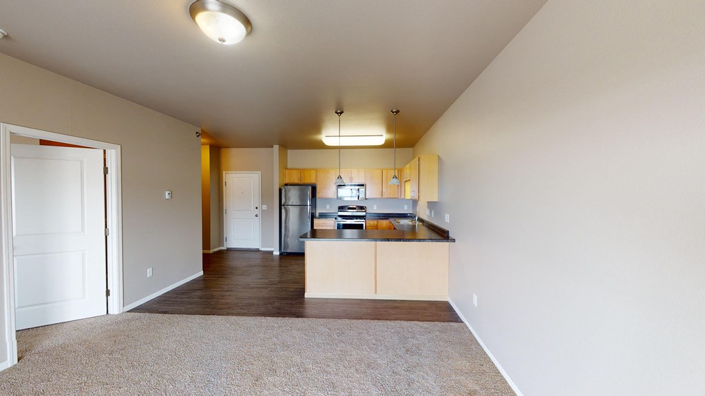 an empty living room with a kitchen with wood flooring