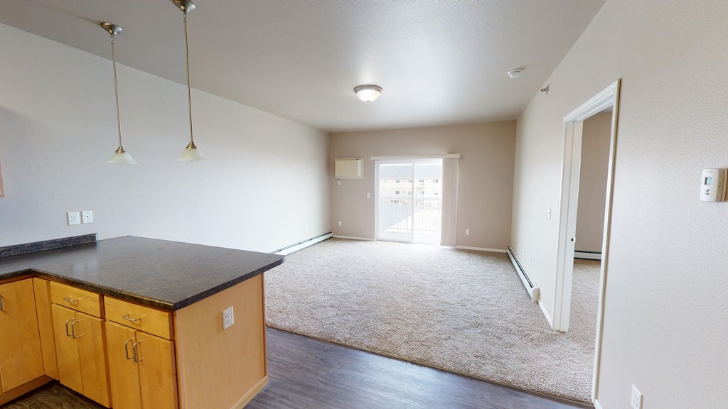 an empty living room with a kitchen and an open door to a bedroom