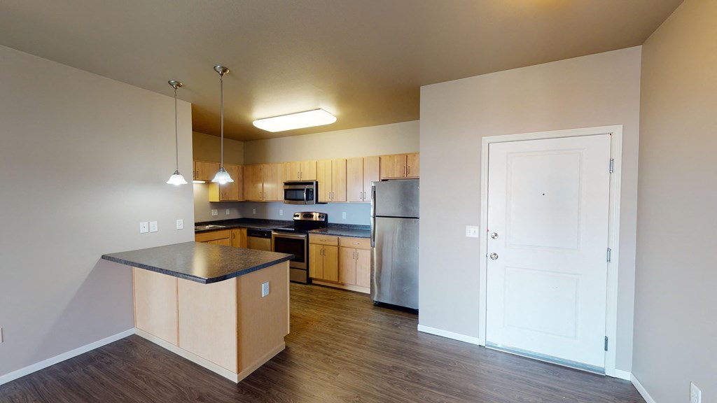 an empty kitchen with wood flooring and a stainless steel refrigerator