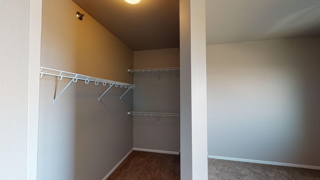 a walk in closet in an empty room with a mirrored wall