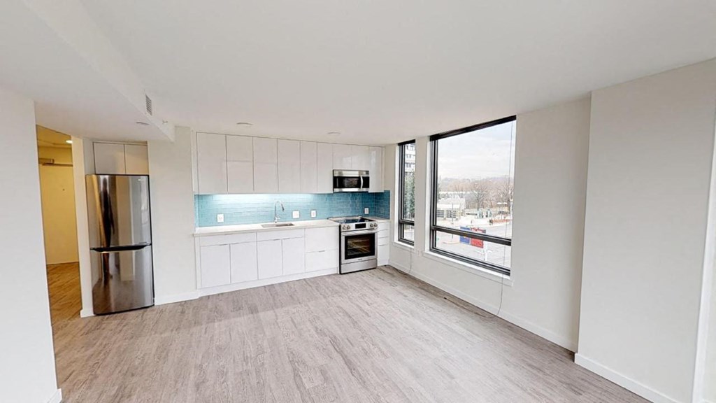an empty living room with a kitchen and a large window