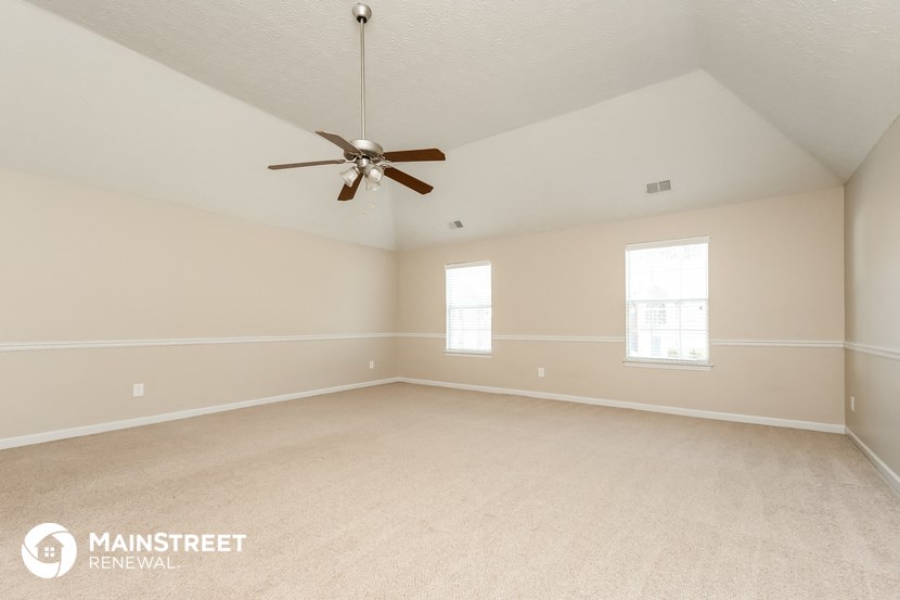 the spacious living room with ceiling fan and carpeting