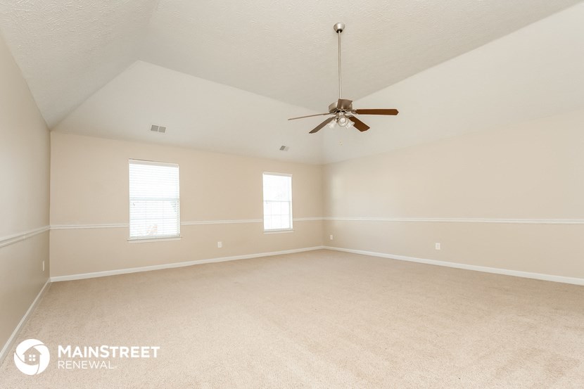 the spacious living room with ceiling fan and carpeting
