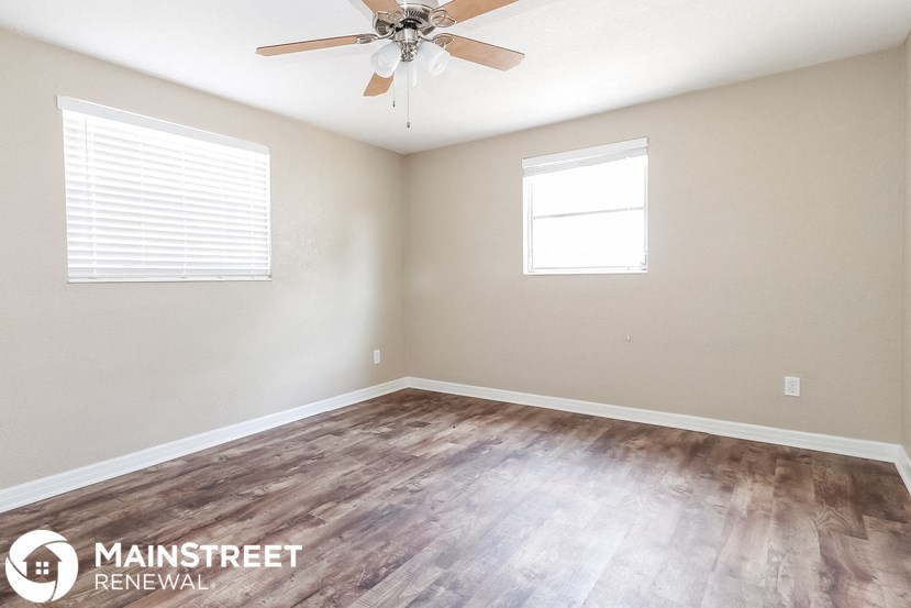 the spacious living room with wood flooring and a ceiling fan