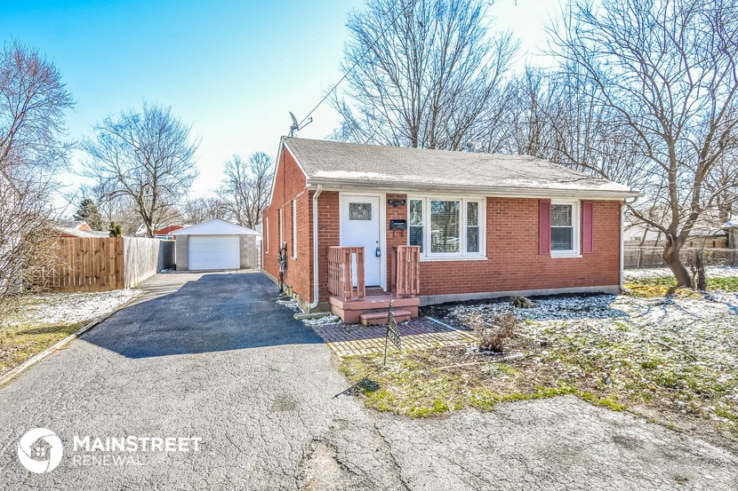 a small brick house with a driveway and a fence