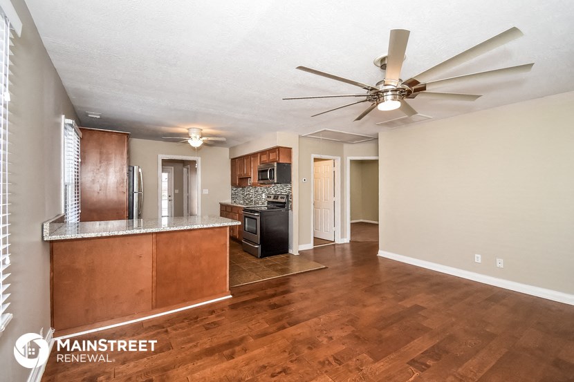 the living room and kitchen of an apartment with wood floors and a ceiling fan