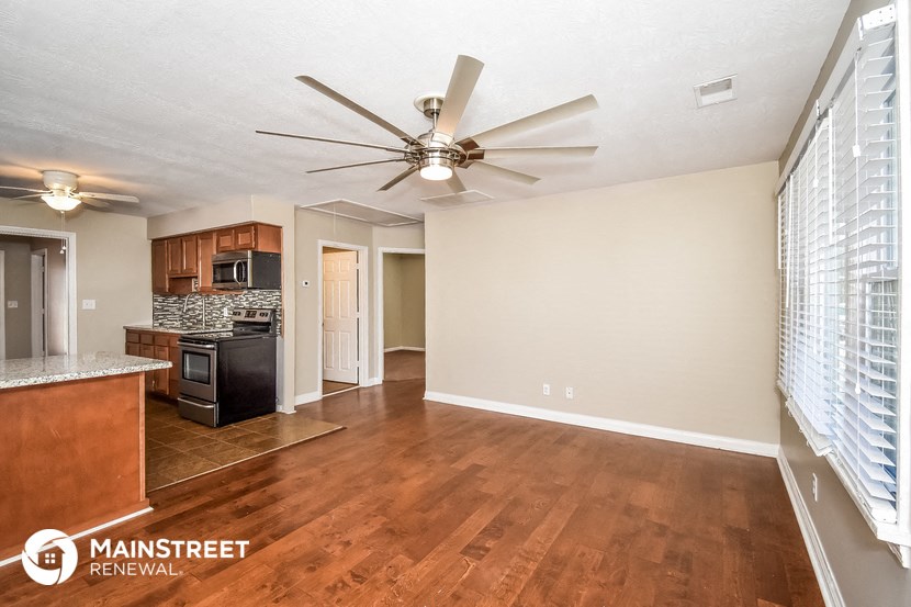 the spacious living room and kitchen with wood flooring and a ceiling fan