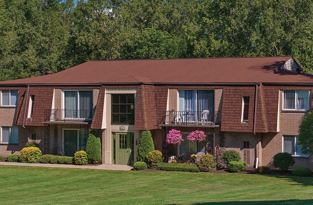 A large building with a green door and windows surrounded by bushes and trees.