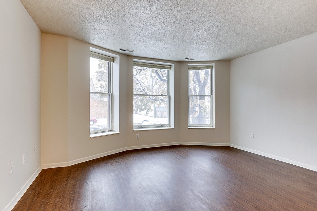 an empty living room with three windows and wood floors