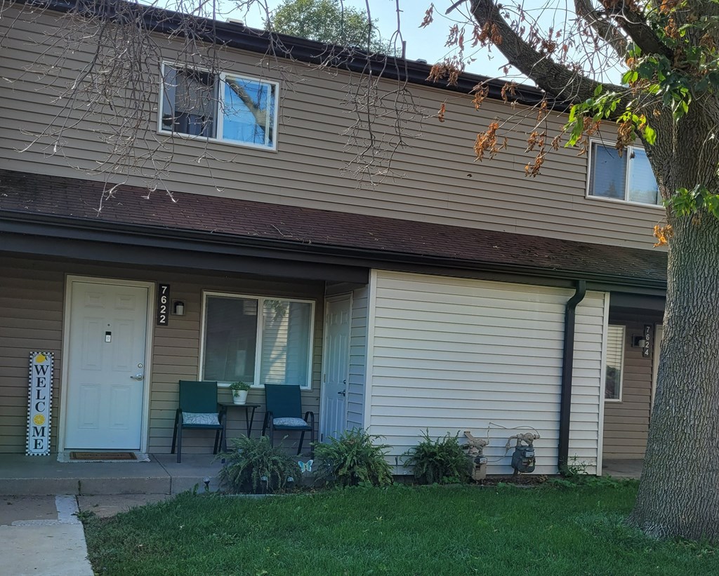 the front of a tan house with a porch and a white door