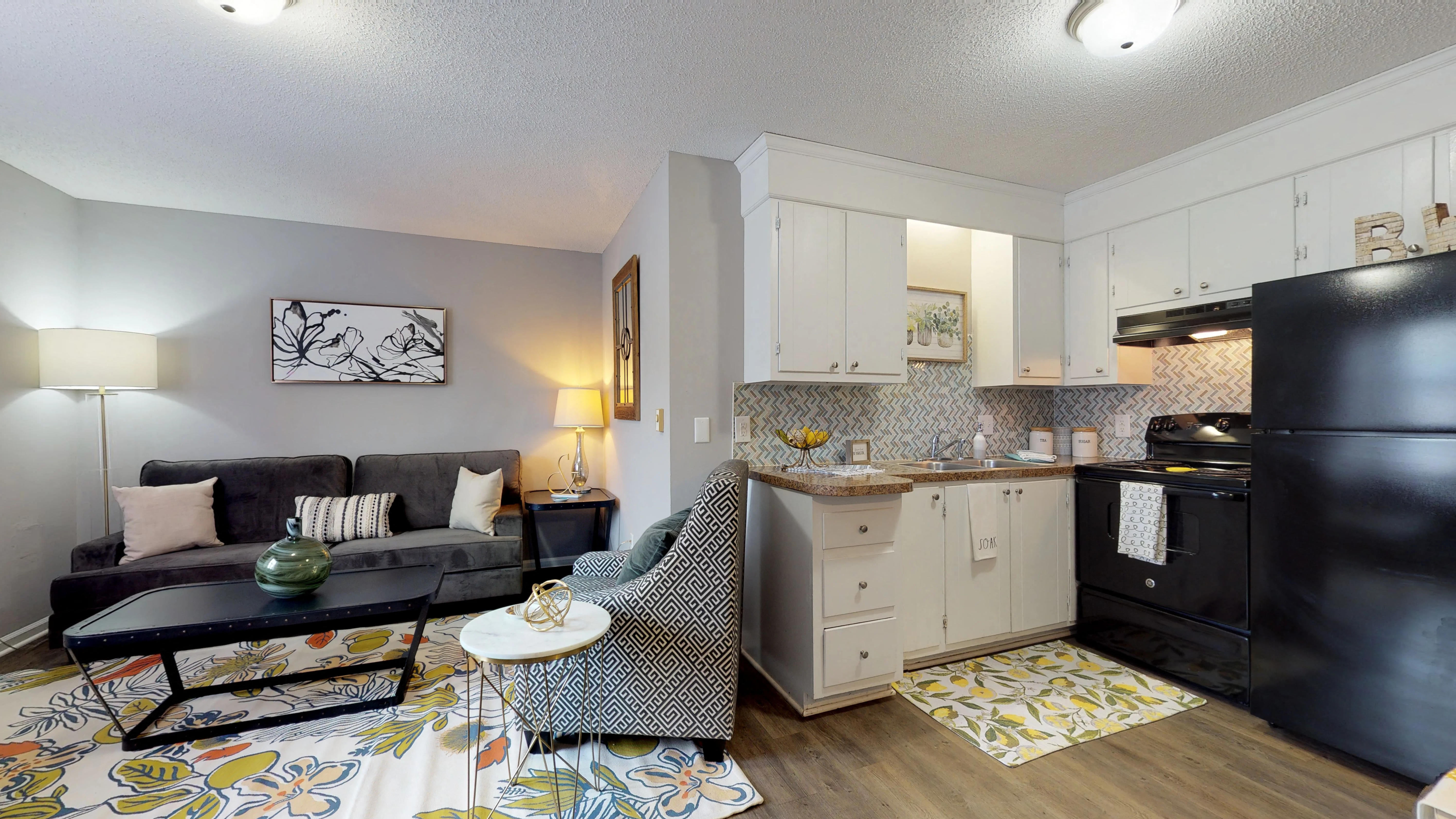 A black fridge sits in a kitchen with white cabinets and a black couch with pillows.