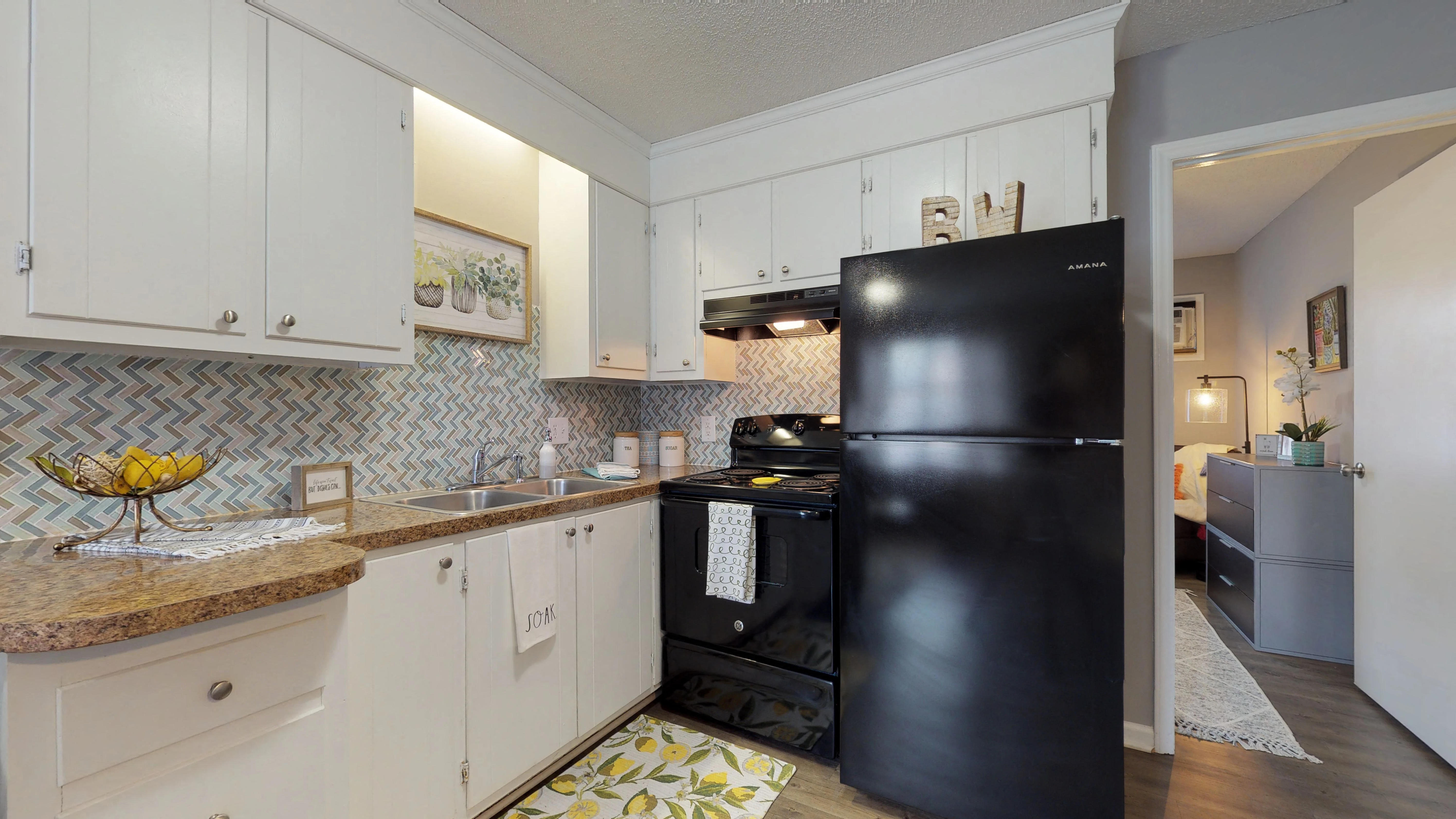 A black refrigerator in a kitchen with white cabinets.