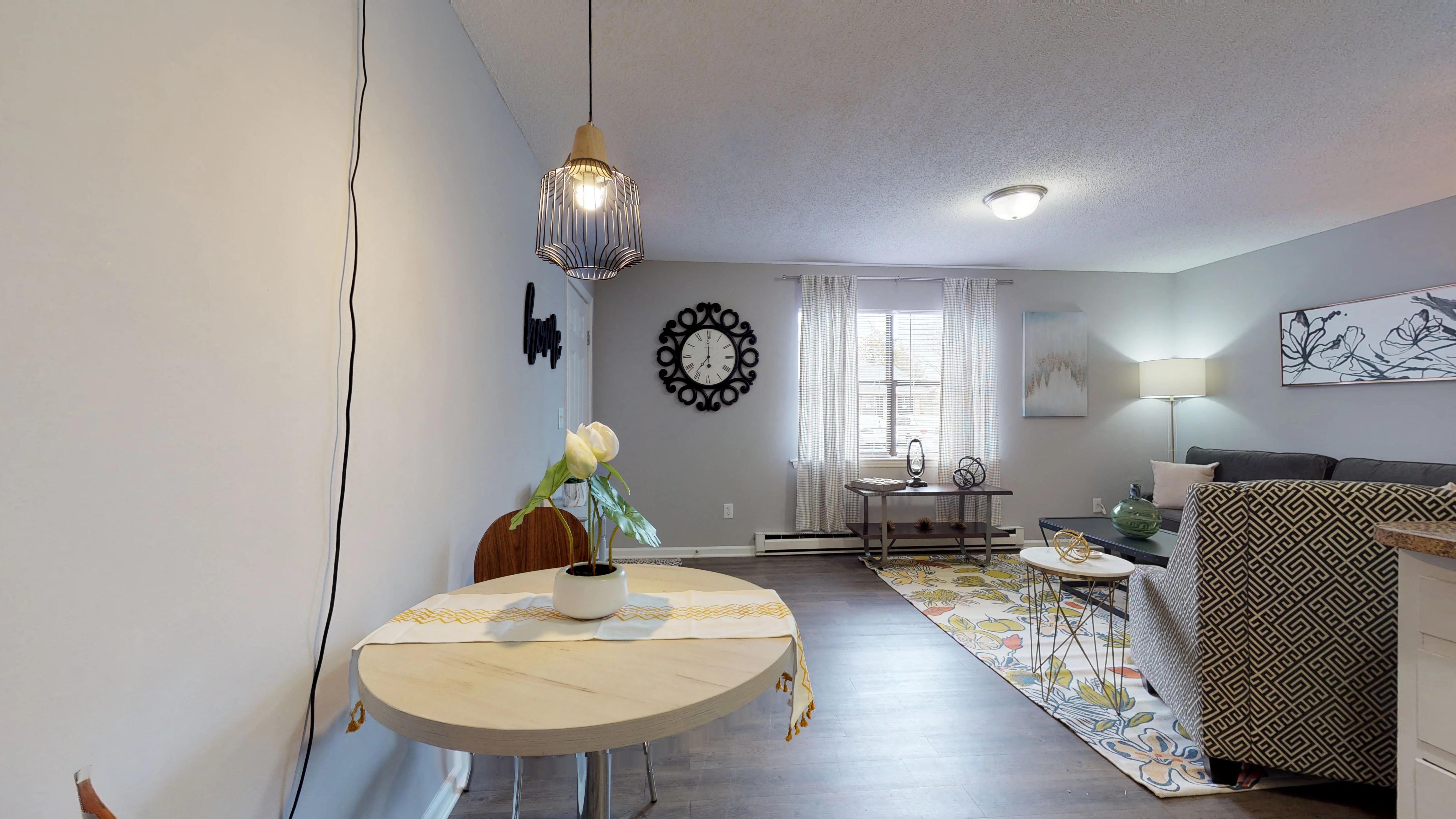 A living room with a table, chairs, and a clock on the wall.