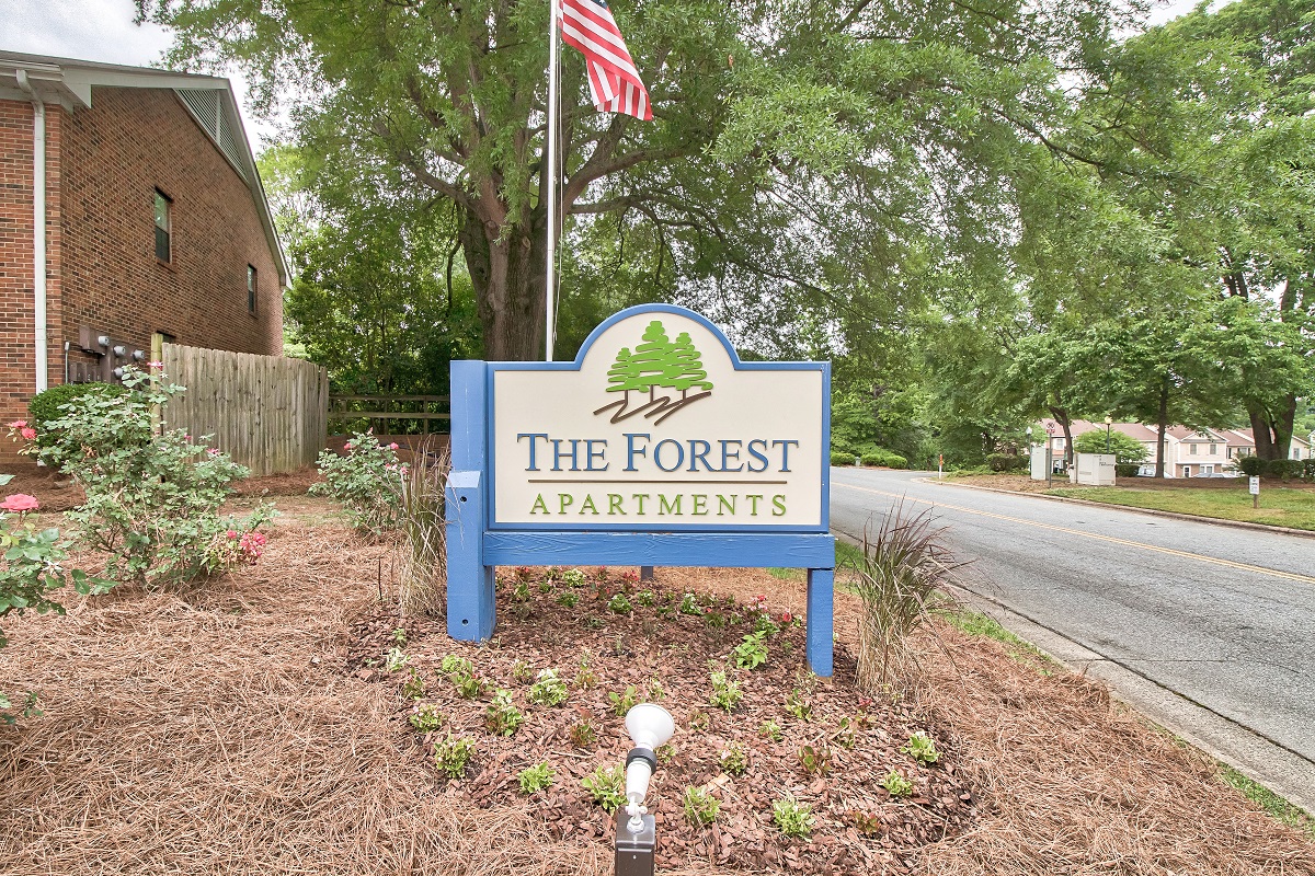 a sign for the forest apartments on the side of a road