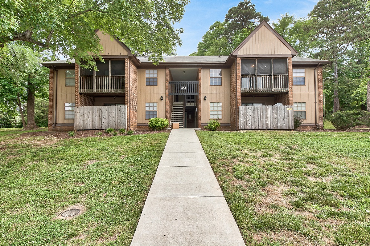 a sidewalk in front of an apartment building with grass and trees