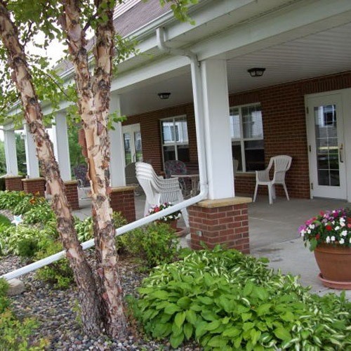 a porch with two white chairs and a tree
