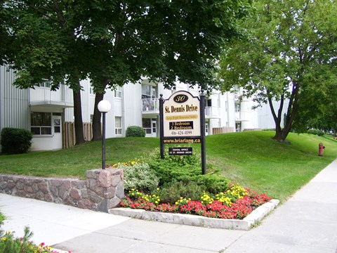 A sign for St. Denis Drive is surrounded by flowers and greenery.