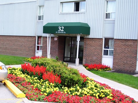 A flower bed in front of a building with a green awning that says 32 St Dennis.