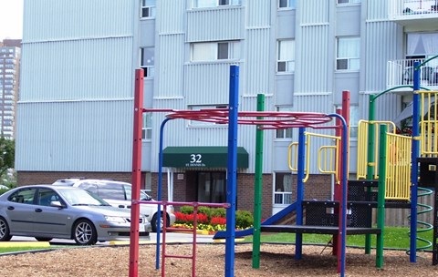 A playground with a red and blue structure in front of a building with the number 32 on it.
