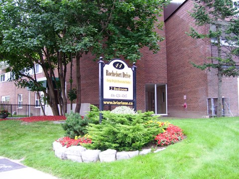 A sign for Rochefort Drive is in front of a brick building.