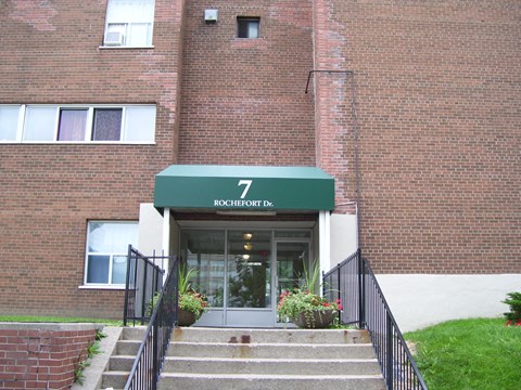 A brick building with a green awning that says 7 Rochefort Dr.