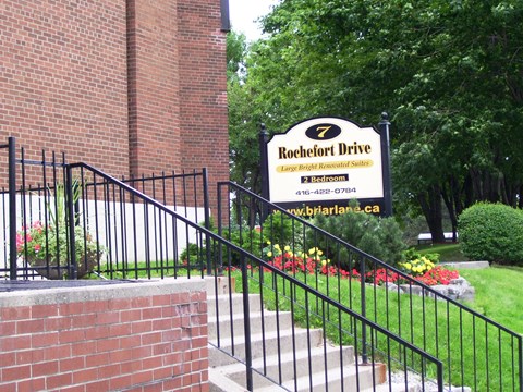 A sign for Rochefort Drive is displayed in front of a brick building.