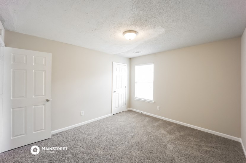 the spacious living room with carpet and a door to the bedroom