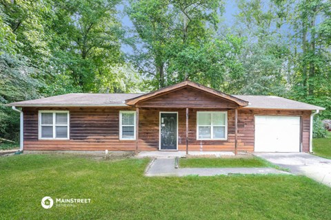 front view of a log cabin with a lawn and trees