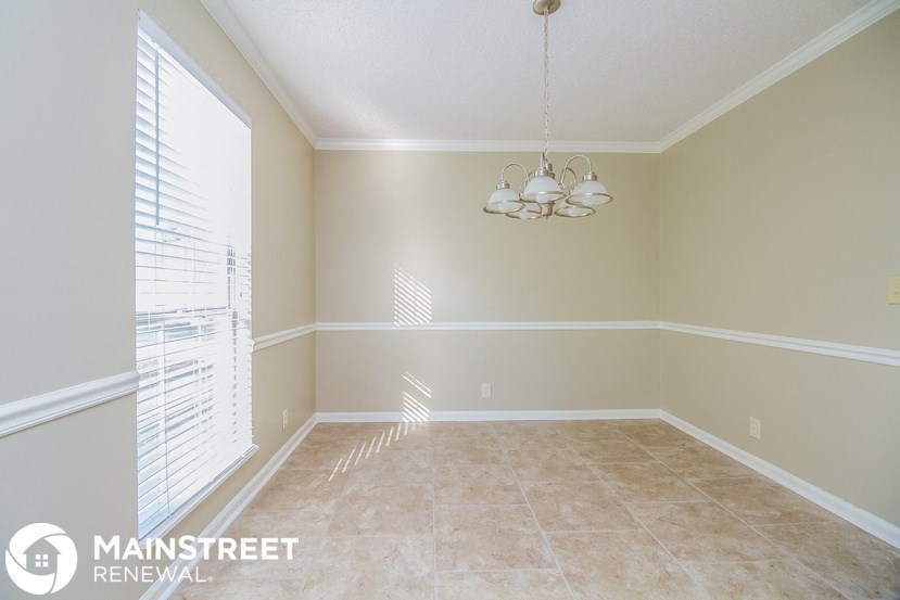 an empty dining room with a window and a chandelier