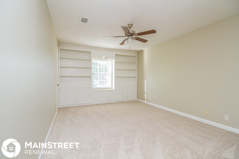 an empty living room with a ceiling fan and white shelves