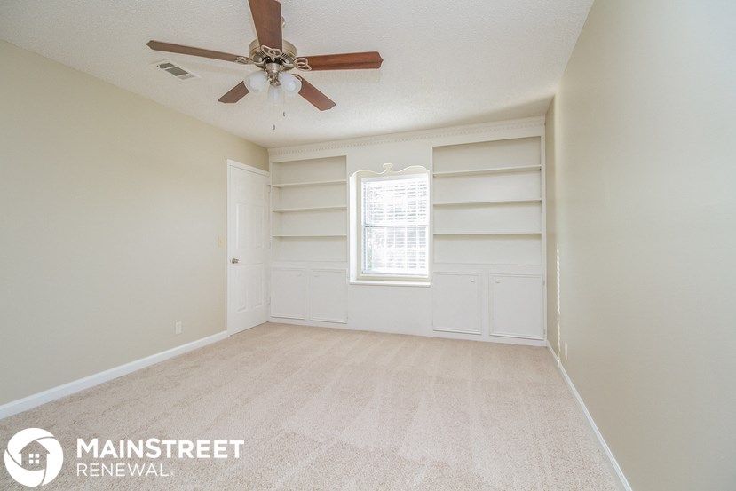 an empty living room with a ceiling fan and white shelves