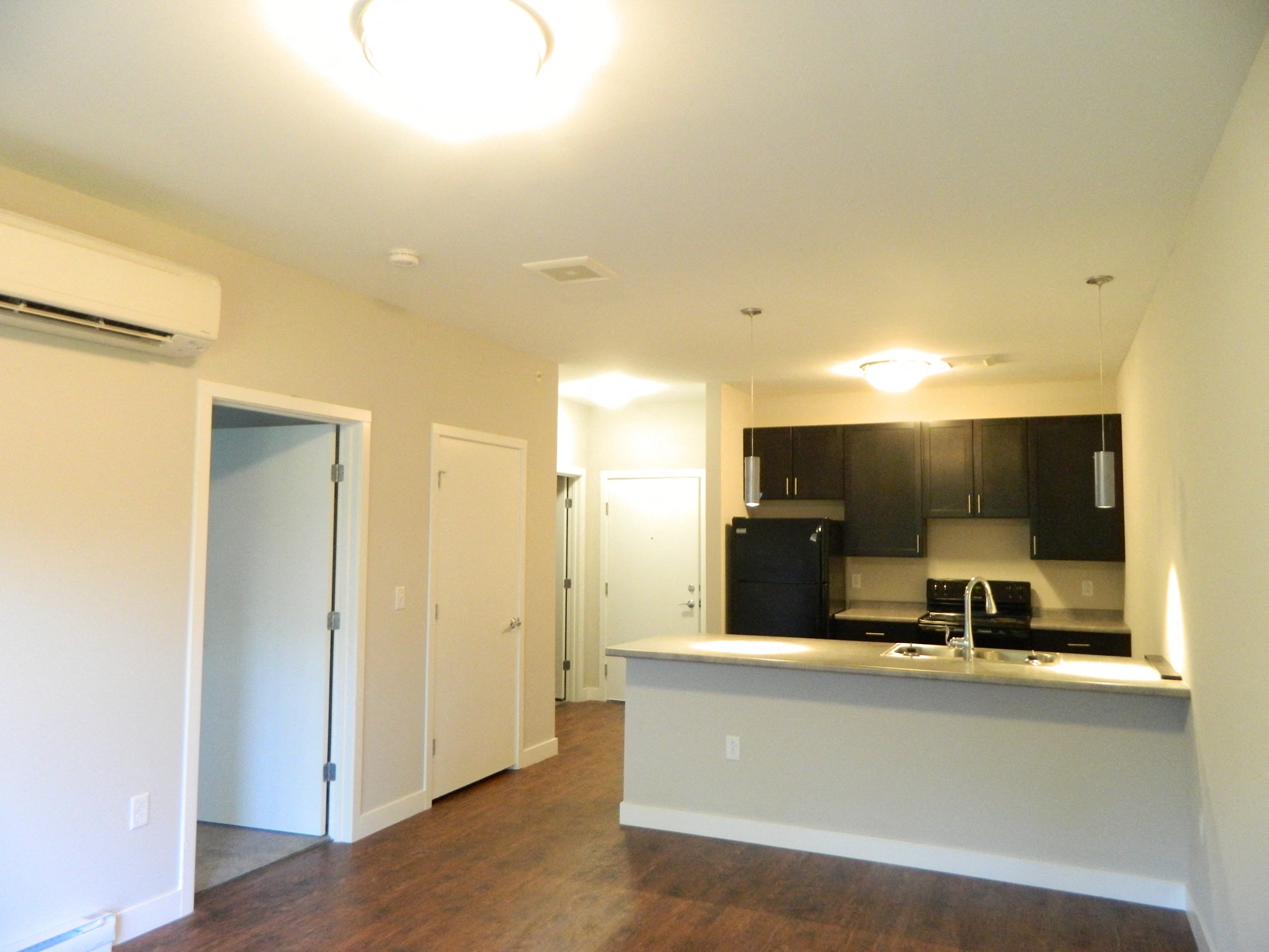 an empty living room with a kitchen and a door to a hallway
