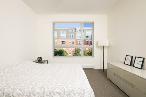 Room with bed, lamp, and dresser with window overlooking Winooski Falls Way