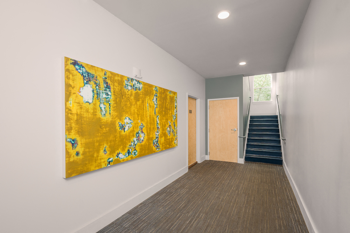 a large yellow painting on a wall in a hallway with stairs